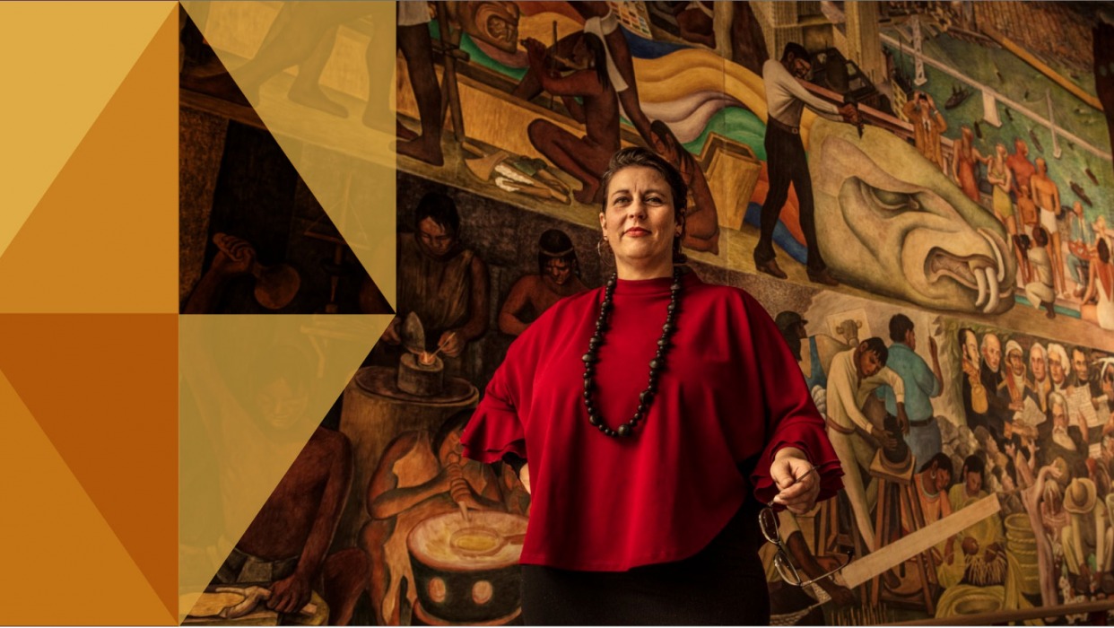 Professor stands in front of Diego Rivera Mural