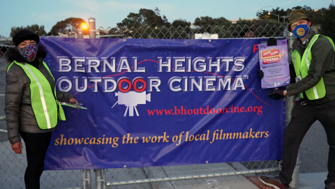 Two people holding banner "BERNAL HEIGHTS OUTDOOR CINEMA"
